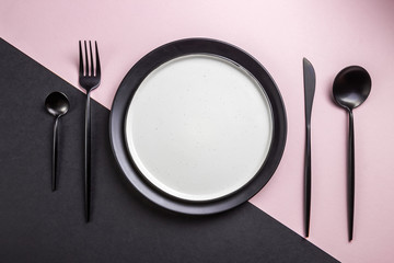 Black setting: plates, inen napkin and silverware on pink and black background. Top view.