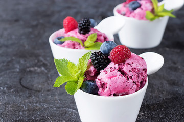 Homemade berry sorbet in white cups and fresh berries on a black background.