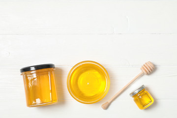 Glass jar and bowl with honey, dipper on white wooden background. Flat lay