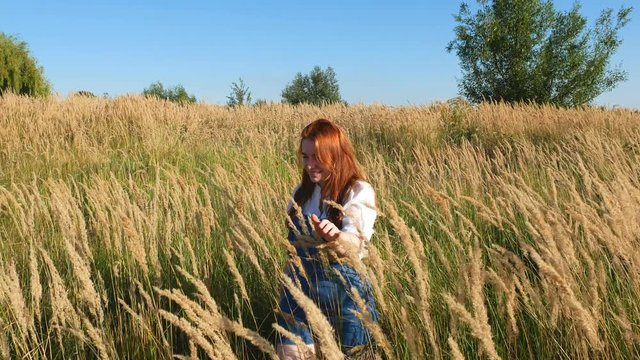 red-haired girl in blue overalls in a field of spikelets