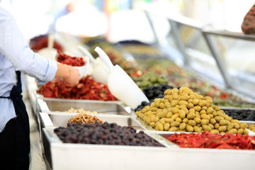 Sprzedawca pakuje oliwki na straganie, w markecie, na rynku miasta Wocław.