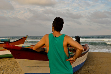 Man with green t-shirt leaning on a boat on the beach at sunset