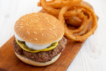 Homemade Mississippi Slug Burger with onion rings on a rustic wooden board on a white wooden surface, side view. Close-up.