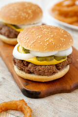 Homemade Mississippi Slug Burger with onion rings on a rustic wooden board, side view. Closeup.