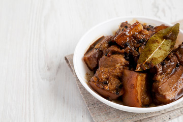 Homemade Filipino Adobo Pork in a bowl on a white wooden surface, side view. Space for text.