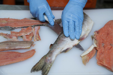 professional cutting of raw red salmon fish. Hands with a knife close-up. Fish factory, shop, production, restaurant.