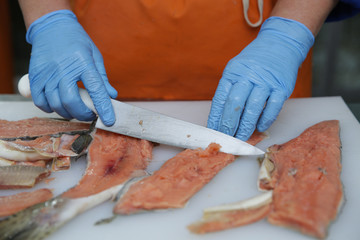 professional cutting of raw red salmon fish. Hands with a knife close-up. Fish factory, shop, production, restaurant.