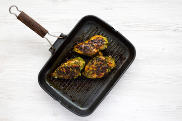 Grilled chimichurri chicken breast in a grilling pan over white wooden background, top view. Flat lay, overhead, from above. Copy space.