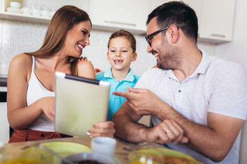 Family eating breakfast at kitchen table using digital tablet