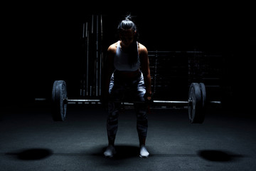 Fototapeta na wymiar Female bodybuilder make her workout with weights - barbell. Light from above, dark background.