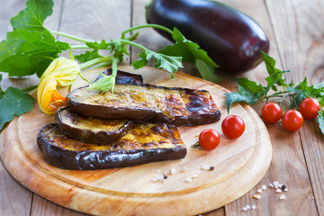 Slices of eggplant roasted on a grill, served with cherry tomato on a wooden board. Healthy vegetarian food.