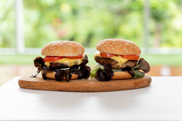 Two hamburgers placed on a wooden tray on a white table with green blurred soft background, to food concept.