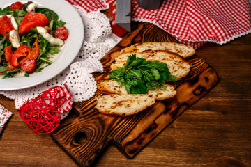 tomatoes, peppers and greens on a white plate and slices of bread with herbs on a wooden tray