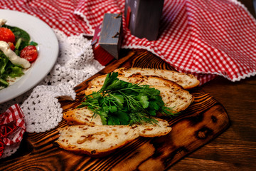 tomatoes, peppers and greens on a white plate and slices of bread with herbs on a wooden tray