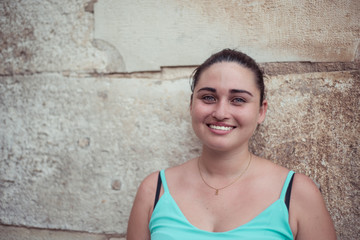 Brunette girl smiles and looks towards the camera. Copy space. Historical stone background.
