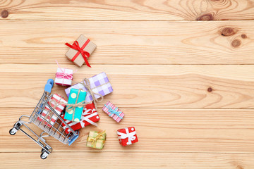 Small shopping cart with gift boxes on brown wooden table