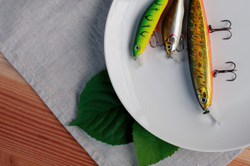Colored fish bait  with sharp fishing hooks lies on a white plate on a wooden table