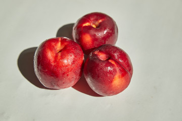 Three beautiful ripe, juicy nectarines lie on a white table.