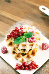 Traditional belgian waffles with fresh mint, sugar and raspberries on table