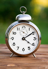 Retro alarm clock on a wooden table in the summer garden.Vertical.