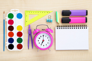 School supplies with pink alarm clock on brown wooden table