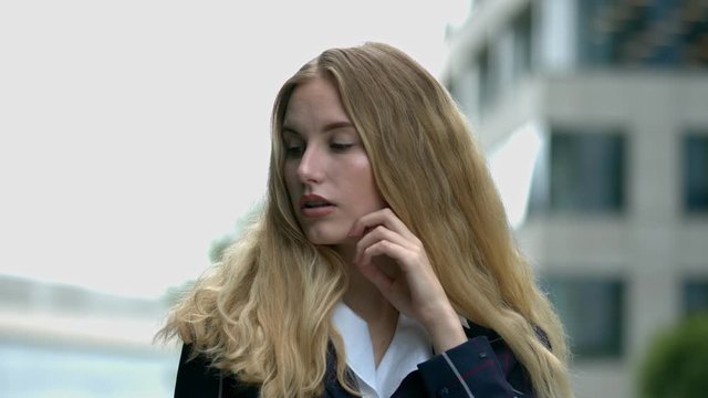 A pretty young blonde woman poses, outdoors in an urban setting