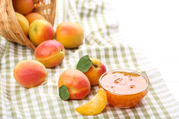 Jam in bowl and apricots on white wooden table