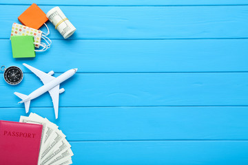 Airplane model with passport, dollar banknotes, compass and paper shopping bags on blue wooden table