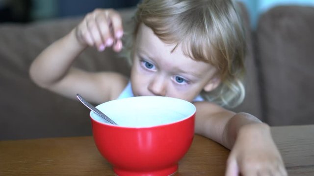 Cute little adorable naughty boy having cereal from a bowl for breakfast in the kitchen. Child eating breakfast. Bad behavior, eating habbits concept. 