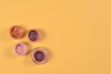 Obraz na płótnie Canvas Cosmetics. Makeup. Jars with crumbly bright shadows, glitter. Pink,peach, golden colors on beige background. Closeup. Space for text or design.
