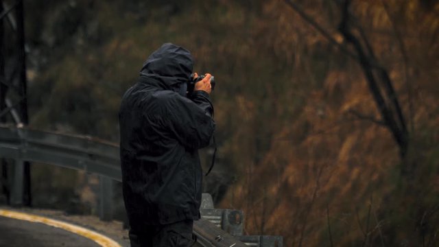 Photographer standing on the side of the road in the rain taking pictures of nature and the landscape.