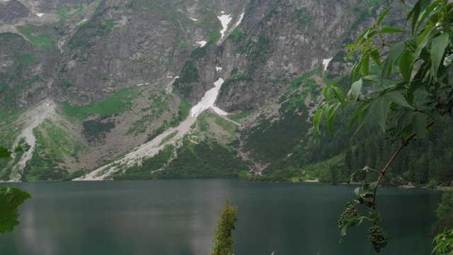 A mountain with a bit of snow near a calm lake. Slow camera pedestal movement. Location: Tatra national park and Morskie oko near Zakopane city, Poland.