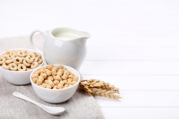 Corn flakes with milk in jar and wheat ears on white wooden table