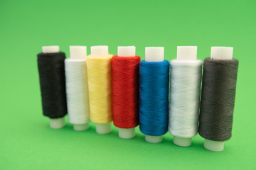 Set of sewing threads beautiful color (blue,yellow, green, white, black) on green background with space for text