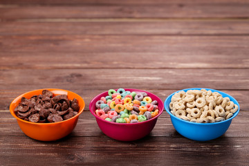 Various corn flakes in bowls on brown wooden table