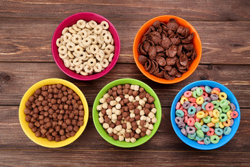 Various corn flakes in bowls on brown wooden table