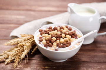 Corn flakes in bowl with milk and wheat ears on brown wooden table