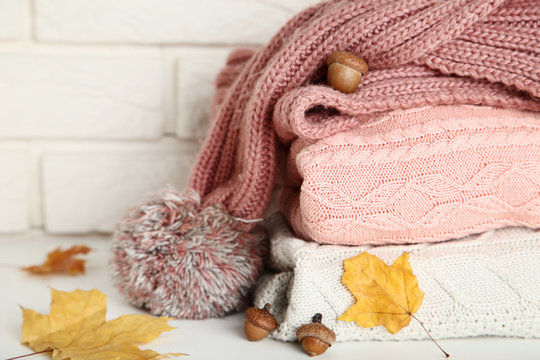 Stack of folded sweaters with scarf, acorns and autumn leafs on brick wall background