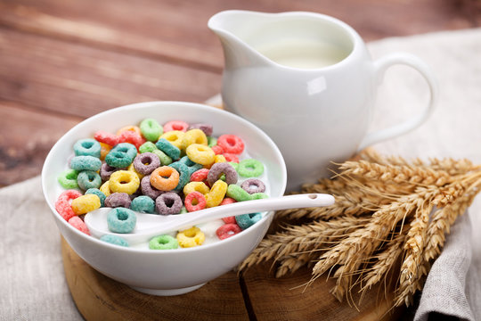 Colorful corn rings in bowl with milk and wheat ears on wooden table