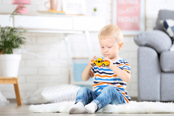 Fototapeta premium Little boy sitting on white carpet at home and playing with car toy