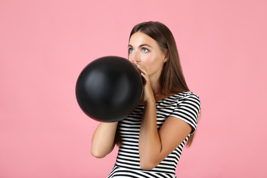 Young Woman Blowing Black Balloon On Pink Background