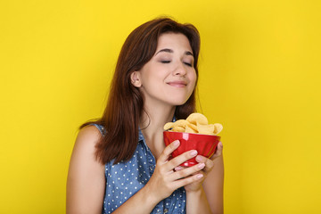 Young woman with potato chips in bowl on yellow background