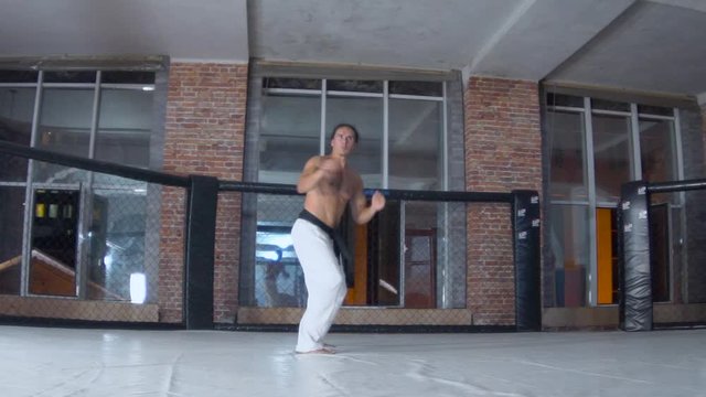 a man with long hair and a strong torso is training, taekwondo, beating his arms and legs in a cage