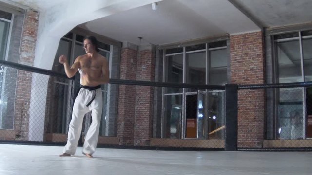 a man with long hair and a strong torso is training, taekwondo, beating his arms and legs in a cage