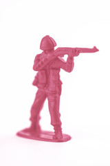 Little pink plastic toy soldier aiming their gun, shot in a white studio.