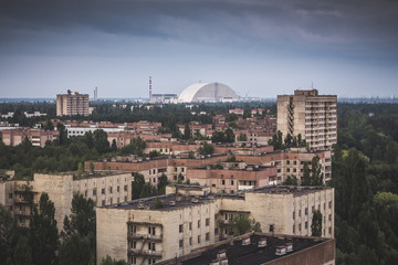 Obraz premium Abandoned uninhabited city overgrown with trees and bushes. A gloomy residential area of a radioactive campus. Nuclear power plant on the horizon.