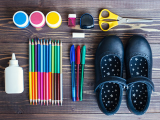 stationery (pens, pencils, glue, sharpener, eraser, scissors) and leather shoes for a girl on a wooden background, top view. September 1st concept and back to school
