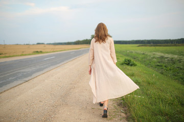 Fototapeta na wymiar Girl walking along the highway. Woman hitchhiking back view.