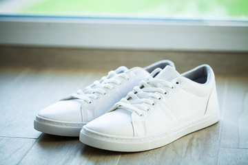 Fototapeta na wymiar Pair of new stylish white sneakers on wood floor.