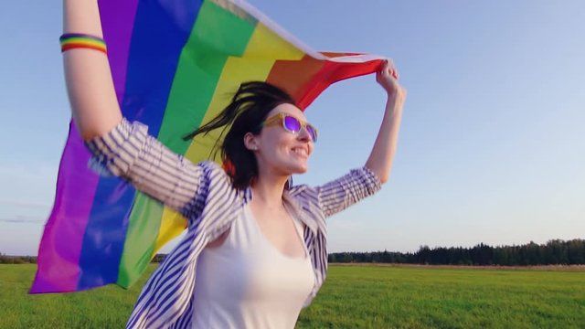Young attractive woman runs across field with LGBT flag slow mo close up